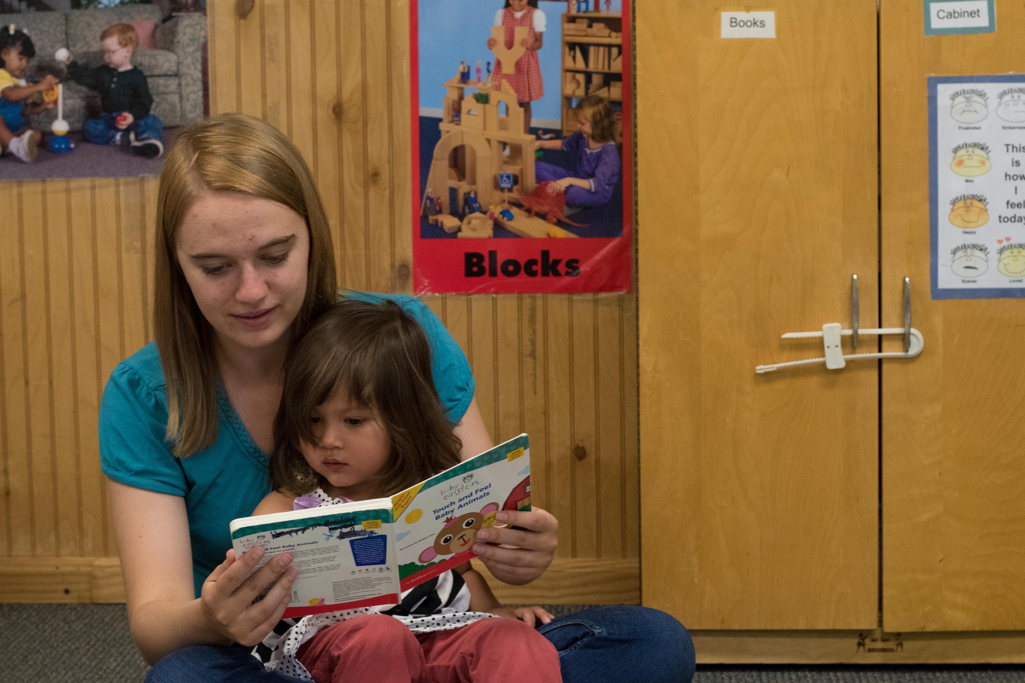 A female ECC teacher reads to a child.